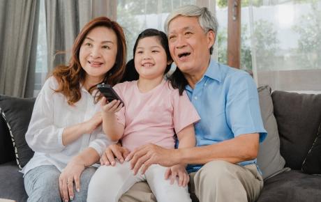 Picture of grandparents on a sofa watching television with their grandchild