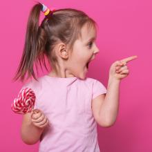 little girl holding lollipop and pointing with an excited smile
